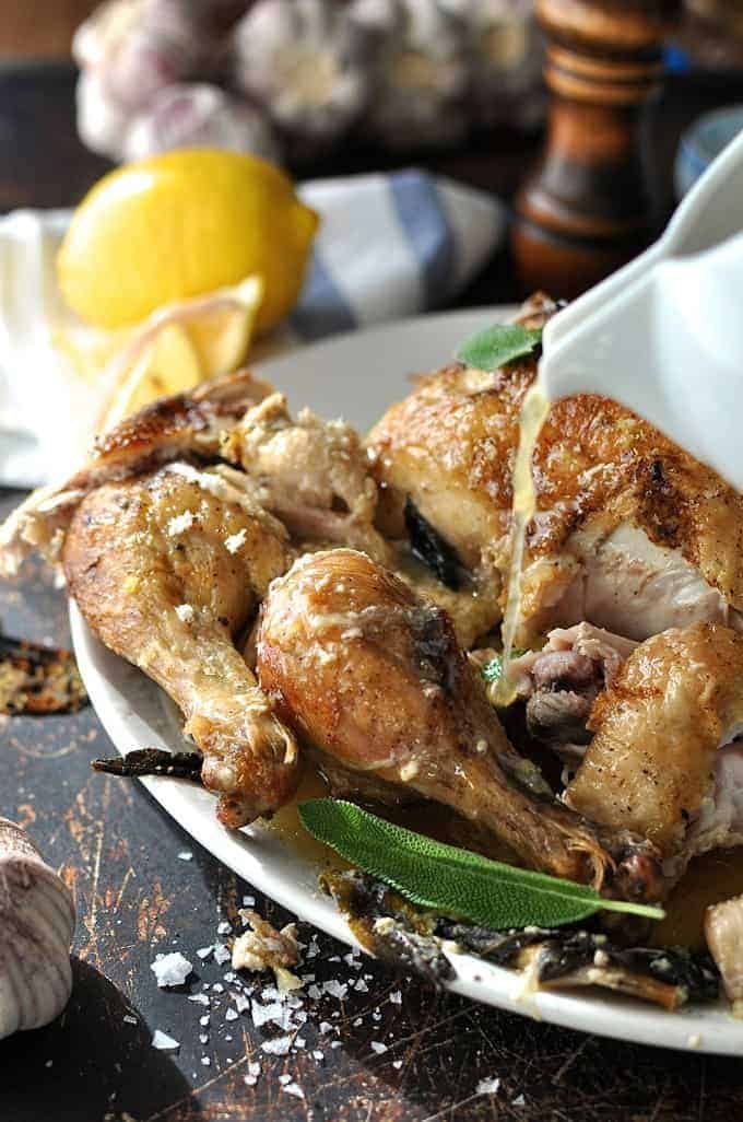 Braising liquid being poured over Chicken in Milk cut up in pieces on a white plate, ready for serving.
