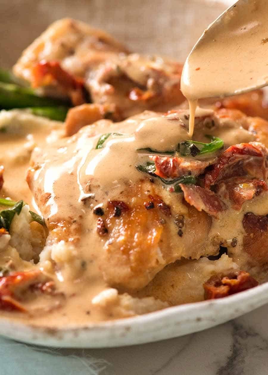 Close up of spoon drizzling creamy Sun Dried Tomato Sauce over chicken