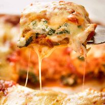 A piece of Vegetarian Lasagna being scooped out of a casserole dish, fresh out of the oven.