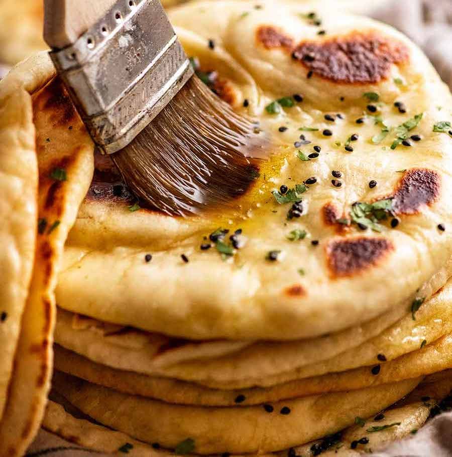 Brushing melted garlic butter on a freshly cooked naan